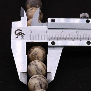 Detailed view measuring a 12mm natural stone bead with a stainless steel caliper
