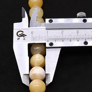 Macro shot of yellow natural stone beads being measured with a silver caliper