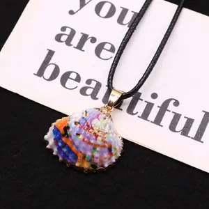Détail du pendentif en coquillage peint à la main avec des bords plaqués or sur fond noir