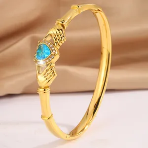Gold open bangle featuring a blue heart-shaped gemstone and crystal accents