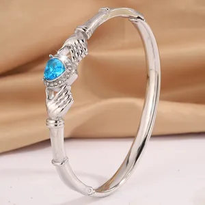 Silver open bangle featuring bamboo texture and heart-shaped blue gem with hand motifs