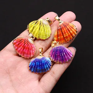 Cinq pendentifs coquillages colorés avec bordure dorée et anneaux métalliques sur une main