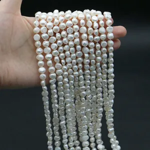 Hand holding strands of white natural freshwater baroque pearls for DIY jewelry making