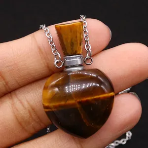 Macro shot of heart-shaped tiger eye stone perfume bottle pendant held in hand
