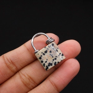 Macro shot of dalmatian jasper stone lock pendant held between fingers with metal ring
