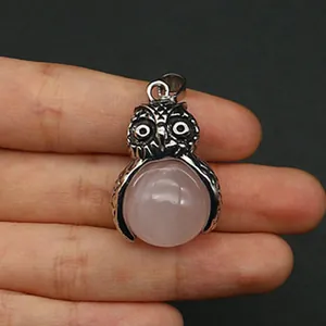 Dettaglio ravvicinato di un ciondolo a gufo in argento con pietra rosa tra le dita