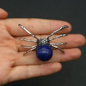 Spider pendant with blue sphere gemstone in silver metal frame held by hand