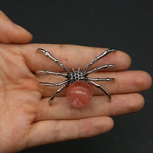 Detailed view of large spider pendant with pink crystal stone held in hand for scale