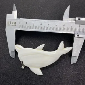 Macro view of white shell dolphin pendant showing length measurement with a caliper