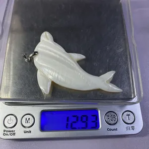 Dolphin-shaped shell pendant with natural pearlescent texture weighing 12.93 grams on a scale