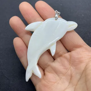 Natural white sea shell dolphin pendant with silver bail shown in hand for size comparison