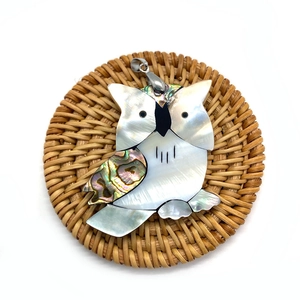 Macro shot of owl pendant made of natural shell and abalone inlay on a rattan mat