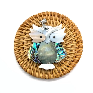Detailed view of owl shell pendant with mother of pearl and abalone inlay on a woven mat