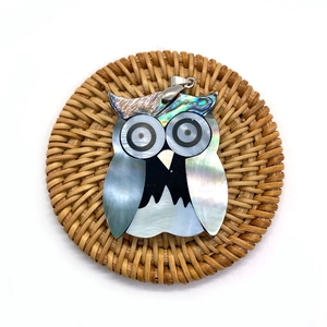 Handcrafted owl-shaped pendant made of abalone shell and white mop on a rattan coaster