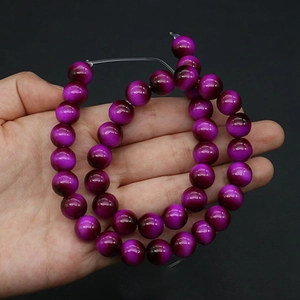 Macro shot of purple cat eye glass beads for DIY jewelry making on hand with black backdrop