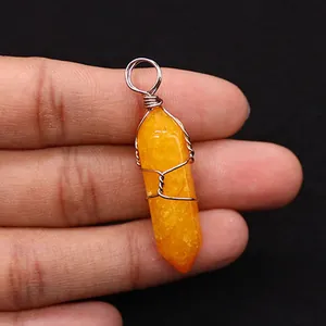 Close-up of yellow hexagonal crystal pendant wrapped in silver wire held by hand