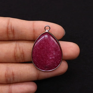 Detailed view of teardrop dyed stone pendant with silver plated edge held by hand