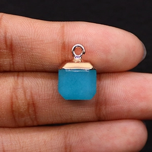 Detail of square faceted blue gemstone pendant with rose gold bail held by hand