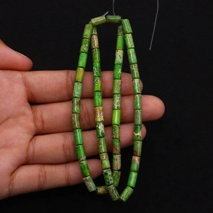 Macro view of green emperor stone cylinder beads with natural veins held in hand
