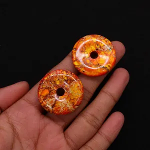 Close-up of two polished orange imperial stone pendants held by hand for size reference