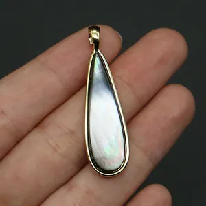 Primer plano de un colgante de gota dorado con nácar irisado en la mano