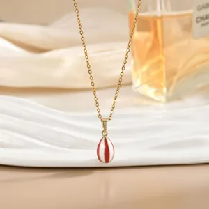 Detalle macro de collar dorado con colgante de gota esmaltado con rayas rojas y blancas