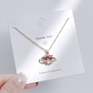 Nahaufnahme der goldenen Halskette mit rosa herzförmigem Kristallanhänger im Saturn-Design