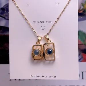 Detail of camera projection necklace pendants with gold chain on a branded display card