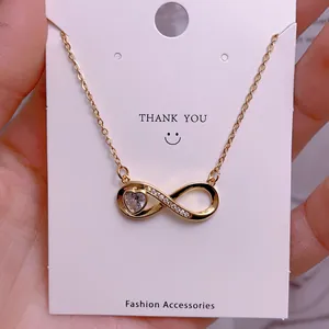 Detail view of gold infinity necklace featuring a heart zircon pendant on white card