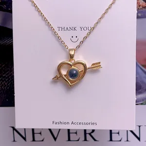 Close-up of golden heart and arrow projection necklace on a white display card