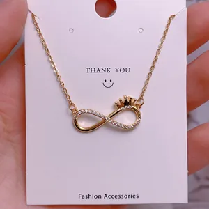 Macro view of gold infinity necklace with crown detail and crystals on display card