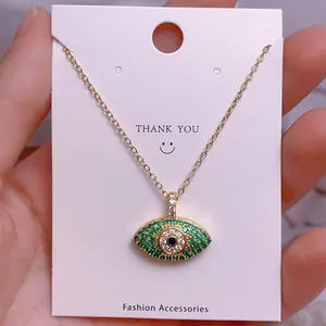 Nahaufnahme der goldenen Evil-Eye-Halskette mit grünen Zirkonia-Steinen auf der Karte