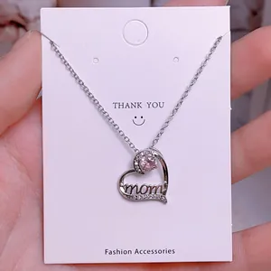Primer plano del collar de corazón con gema rosa y letras mom en tarjeta de joyería