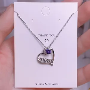 Detalle de collar de corazón plateado con gema púrpura y grabado mom para regalo de madre