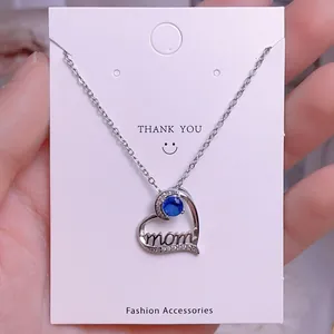 Detalle del colgante corazón con gema azul y letra 'mom' en cadena de plata