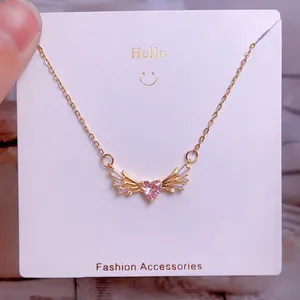 Détail du pendentif ailes d'ange avec cœur rose et cristaux sur chaîne dorée