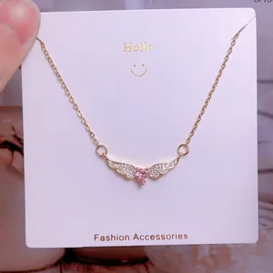 Détail macro du pendentif ailes de cœur doré avec pierre rose et diamants blancs