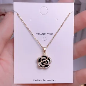 Detalle de collar dorado con colgante de camelia en esmalte negro y microdiamantes finos