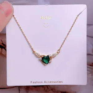 Vue macro du collier en or avec pendentif émeraude en cœur et ailes serties