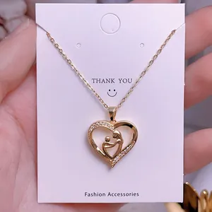 Detalle del collar corazón dorado con silueta de madre e hijo en tarjeta de moda