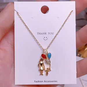 Detalle del collar con colgante de corazón dorado con silueta de madre e hijo y globos