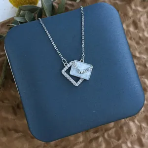 Détail macro du pendentif enveloppe en émail blanc et incrustation de zircon