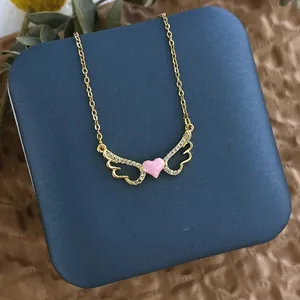 Détail d'un pendentif ailé plaqué or avec un cœur rose et des pierres en zircone