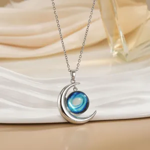 Detail van zilveren halve maan ketting met blauwe sterrennevel bol op zijden ondergrond