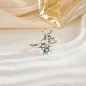 Detail view of cz starfish and blue enamel sea turtle ring on elegant white wavy tray