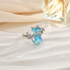 Dettaglio anello a gatto argento con pietre azzurre su supporto bianco a onde