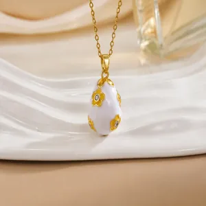 Close-up of gold 18K plated egg pendant with white enamel floral detail and zircon crystals