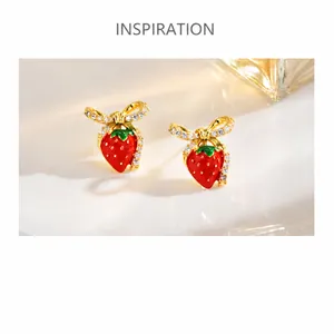 Macro view of strawberry earrings with red enamel and pavé bow details on a tray