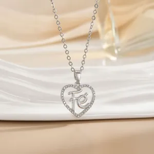 Close-up of silver heart necklace with Fe letter engraving on white porcelain