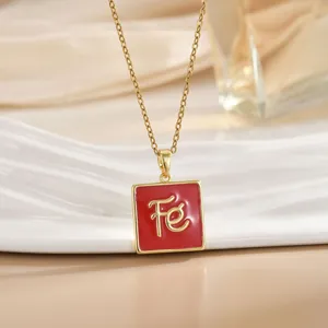 Detail view of gold cross chain necklace with red enamel square pendant and Fe letter charm